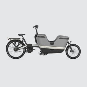 Open image in slideshow, A side view image of the Gazelle Makki HMB cargo ebike, showing the full length of the bike. At the rear is a pannier rack with bungee strap, and a belt drive providing less maintenance and quieter riding. The high EPP box is suitable for carrying two children with safety belts or large loads. With a reflector fixed to the rear rack system and an integrated LED lamp on the front, the Makki Load Cargo includes an integrated battery pack and a double kicstand for loading stability. 

